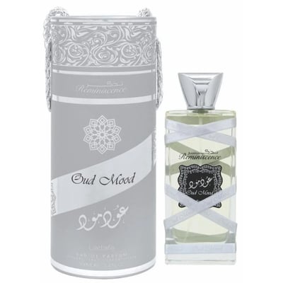 Lattafa Oud Mood Reminiscence 100ml — A cylindrical grey box with silver ornate patterns and a silver ribbon handle stands next to a clear glass perfume bottle with a silver cap, wrapped in white ribbon. | Lattafa Oud Mood Reminiscence 100ml — Kotak kelabu silinder dengan corak perak berhias dan pemegang reben perak