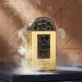 Lattafa Pride Maharjan Gold — A gold perfume bottle with a black mosaic cap and decorative panel sits next to its matching dark green embossed box. | Lattafa Pride Maharjan Gold — Botol minyak wangi emas dengan penutup mozek hitam dan panel hiasan duduk di sebelah kotak hijau gelapnya yang bertebuk.
