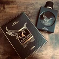 Lattafa Malik Al Tayoor Concentrated 100ml — Black perfume bottle with gold cap and eagle emblem, next to its black and gold patterned box with matching emblem. | Lattafa Malik Al Tayoor Concentrated 100ml — Botol minyak wangi hitam dengan penutup emas dan lambang helang, bersebelahan kotak corak hitam dan emasnya