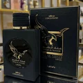 Lattafa Malik Al Tayoor Concentrated 100ml — Black perfume bottle with gold cap and eagle emblem, next to its black and gold patterned box with matching emblem. | Lattafa Malik Al Tayoor Concentrated 100ml — Botol minyak wangi hitam dengan penutup emas dan lambang helang, bersebelahan kotak corak hitam dan emasnya