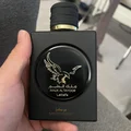 Lattafa Malik Al Tayoor Concentrated 100ml — Black perfume bottle with gold cap and eagle emblem, next to its black and gold patterned box with matching emblem. | Lattafa Malik Al Tayoor Concentrated 100ml — Botol minyak wangi hitam dengan penutup emas dan lambang helang, bersebelahan kotak corak hitam dan emasnya