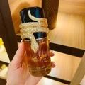 Lattafa Musamam Eau De Parfum 100ml by Lattafa — A golden snake coils around a clear glass perfume bottle filled with amber liquid, next to a textured brown cylindrical case with a snake-skin pattern. | Lattafa Musamam Eau De Parfum 100ml by Lattafa — Ular emas melilit botol minyak wangi kaca jernih berisi cecair