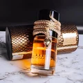 Lattafa Musamam Eau De Parfum 100ml by Lattafa — A golden snake coils around a clear glass perfume bottle filled with amber liquid, next to a textured brown cylindrical case with a snake-skin pattern. | Lattafa Musamam Eau De Parfum 100ml by Lattafa — Ular emas melilit botol minyak wangi kaca jernih berisi cecair