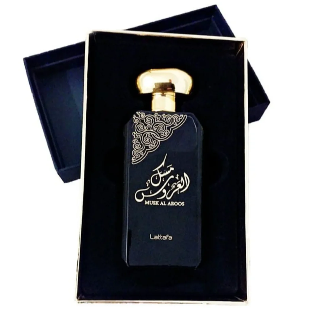 Lattafa Musk Al Aroos — A dark blue perfume bottle with gold Arabic calligraphy and 'MUSK AL AROOS LATTAFA' text, presented in an open dark blue gift box with a black velvet insert. | Lattafa Musk Al Aroos — Botol minyak wangi biru gelap dengan kaligrafi Arab emas dan teks 'MUSK AL AROOS LATTAFA', dipersembahkan dalam
