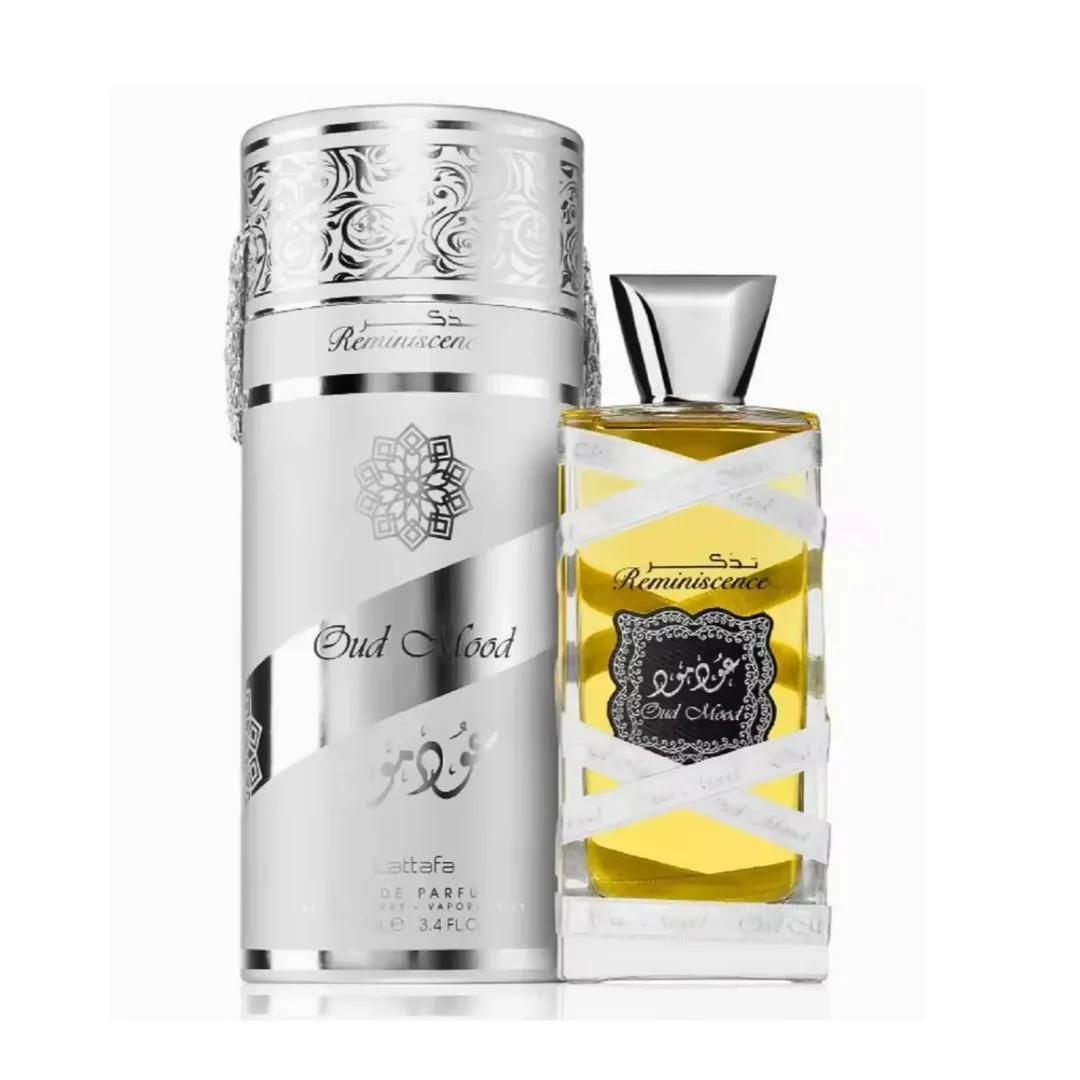Lattafa Oud Mood Reminiscence 100ml — A cylindrical grey box with silver ornate patterns and a silver ribbon handle stands next to a clear glass perfume bottle with a silver cap, wrapped in white ribbon. | Lattafa Oud Mood Reminiscence 100ml — Kotak kelabu silinder dengan corak perak berhias dan pemegang reben perak