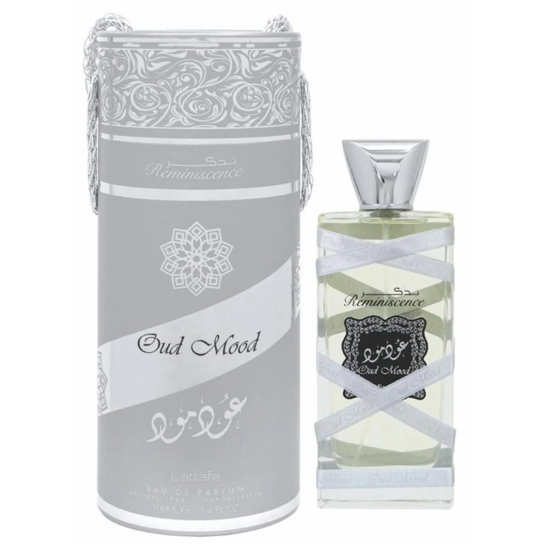Lattafa Oud Mood Reminiscence 100ml — A cylindrical grey box with silver ornate patterns and a silver ribbon handle stands next to a clear glass perfume bottle with a silver cap, wrapped in white ribbon. | Lattafa Oud Mood Reminiscence 100ml — Kotak kelabu silinder dengan corak perak berhias dan pemegang reben perak