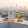 Afnan 9 AM by Afnan 100 ml EDP Unisex — yellow glass bottle, gold cap, white box, citrus fruit, blurred cityscape