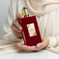 Woman holding Ameerat Al Arab Lattafa red fragrance hands closeup side angled