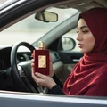 Woman in hijab holding Ameerat Al Arab Lattafa red fragrance car interior closeup
