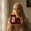 Woman in hijab holding Ameerat Al Arab Lattafa women fragrance packaging low light
