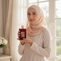 Woman in hijab holding Ameerat Al Arab Lattafa red gold fragrance closeup front