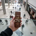 Hand holding Asad Bourbon Lattafa brown fragrance shopping mall background high above
