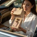 Woman holding Eclaire Lattafa edp in car seat showing pink gold packaging open