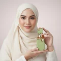 Woman in hijab holding Eclaire Pistache Lattafa green gold unisex fragrance closeup
