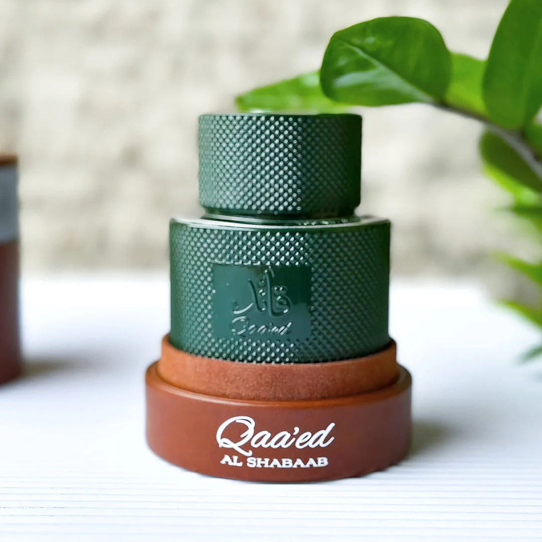 Qaaed Al Shabaab Lattafa green cologne wooden base beside plant leaves closeup