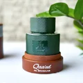 Qaaed Al Shabaab Lattafa green cologne wooden base beside plant leaves closeup