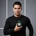 Man holding Qaaed Intense Lattafa green cologne close up grey background black shirt