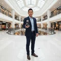 Man in suit holding Lattafa Ramz Silver edp fragrance at shopping mall entrance level floor