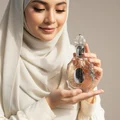 Woman in hijab holding Lattafa Rouat Al Musk pink glass fragrance bottle closeup view side