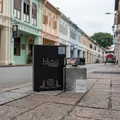 Suqraat Lattafa edp men fragrance black packaging sidewalk beside colorful shophouses street scene