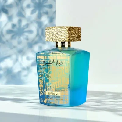 Lattafa Sheikh Al Shuyukh Supreme by Lattafa 100ml — A blue box with Arabic calligraphy and a portrait of a man in a headscarf is next to a clear glass perfume bottle with a gold textured cap and light green liquid. | Lattafa Sheikh Al Shuyukh Supreme by Lattafa 100ml — Kotak biru dengan kaligrafi Arab dan potret