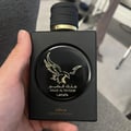 Lattafa Malik Al Tayoor Concentrated 100ml — Black perfume bottle with gold cap and eagle emblem, next to its black and gold patterned box with matching emblem. | Lattafa Malik Al Tayoor Concentrated 100ml — Botol minyak wangi hitam dengan penutup emas dan lambang helang, bersebelahan kotak corak hitam dan emasnya