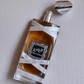 Lattafa Oud Mood Reminiscence 100ml — A cylindrical grey box with silver ornate patterns and a silver ribbon handle stands next to a clear glass perfume bottle with a silver cap, wrapped in white ribbon. | Lattafa Oud Mood Reminiscence 100ml — Kotak kelabu silinder dengan corak perak berhias dan pemegang reben perak