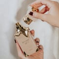 Hands holding Eclaire Lattafa beige gold fragrance Malaysia white background closeup