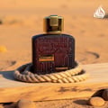 Lattafa Ramz Gold Woman perfume bottle on wooden plank surrounded by rope sand pebbles closeup view