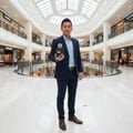 Man in suit holding Lattafa Ramz Silver edp fragrance at shopping mall entrance level floor