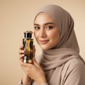 Woman in hijab holding Teriaq Intense Lattafa eau de parfum gold brown glass elegant closeup portrait