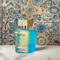 Lattafa Sheikh Al Shuyukh Supreme by Lattafa 100ml — A blue box with Arabic calligraphy and a portrait of a man in a headscarf is next to a clear glass perfume bottle with a gold textured cap and light green liquid. | Lattafa Sheikh Al Shuyukh Supreme by Lattafa 100ml — Kotak biru dengan kaligrafi Arab dan potret