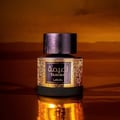 Lattafa Tamima 100ml Eau de Parfum — A black perfume bottle with a wooden cap and a rose gold label sits next to its matching black textured box with rose gold Arabic calligraphy and text. | Lattafa Tamima 100ml Eau de Parfum — Botol minyak wangi hitam dengan penutup kayu dan label emas mawar duduk bersebelahan dengan